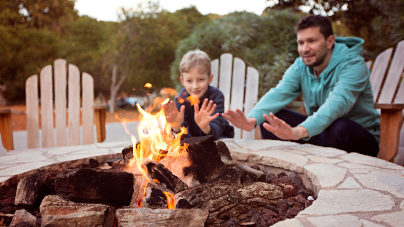 Stay cozy all winter with an outdoor fireplace - man and boy warming hands at the fire